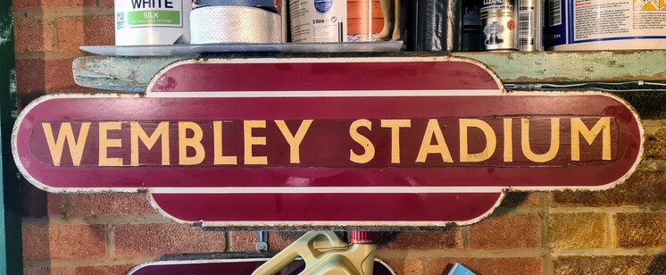 A sign from the railway station Wembley Stadium in maroon with gold lettering.